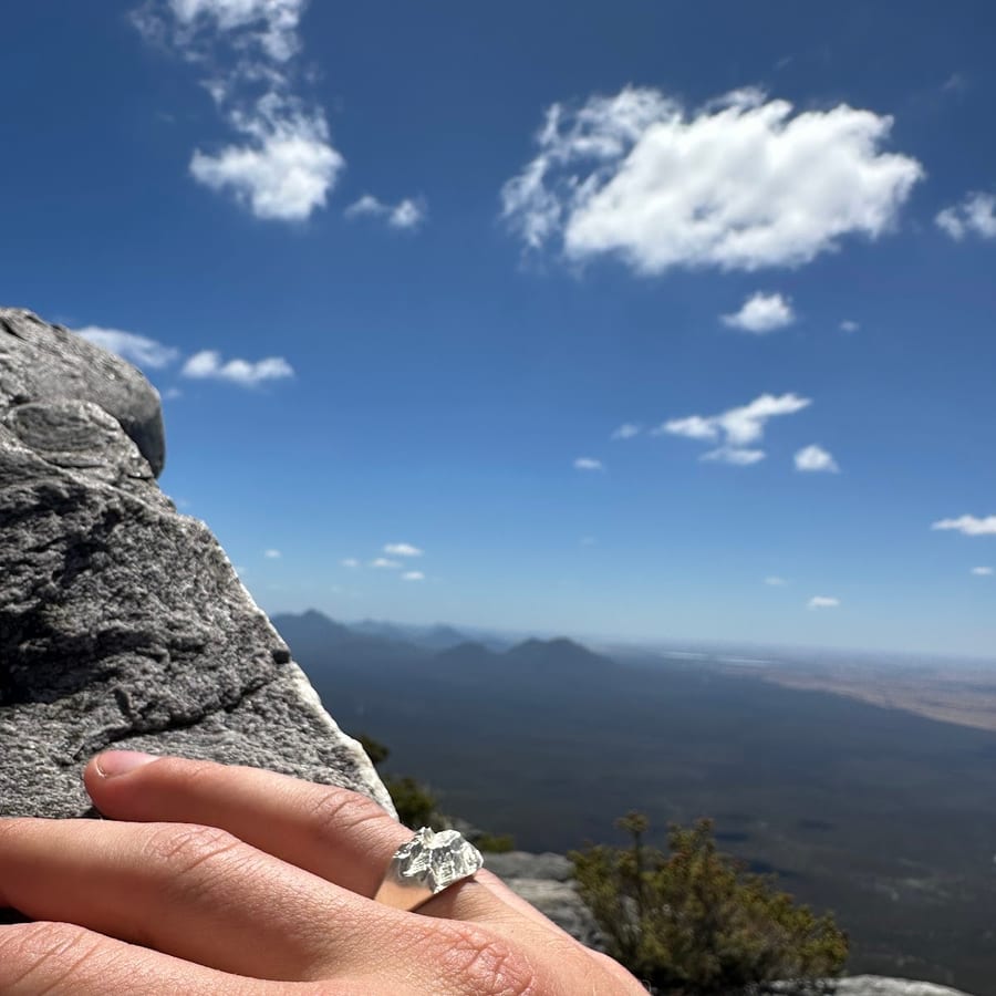 Bague montagne en argent portée en randonnée, main sur un rocher face aux sommets, avis client
